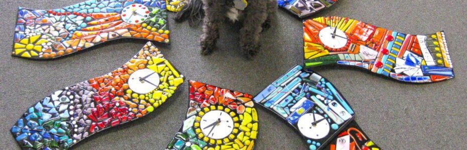 A small dog surrounded by colorful mosaic art pieces shaped like socks.